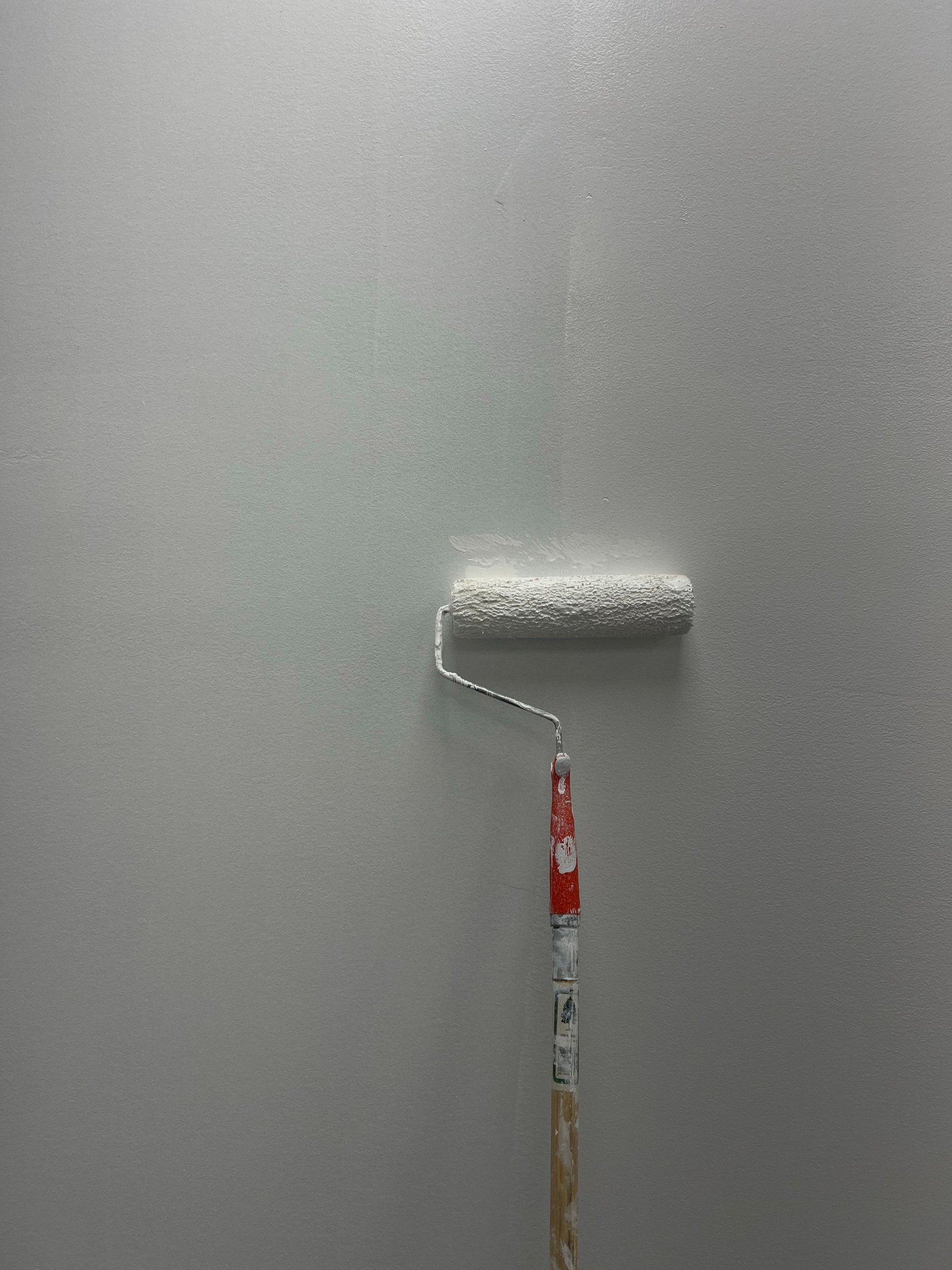 Farbroller mit orangefarbenem Stiel an einer frisch gestrichenen, hellgrauen Wand